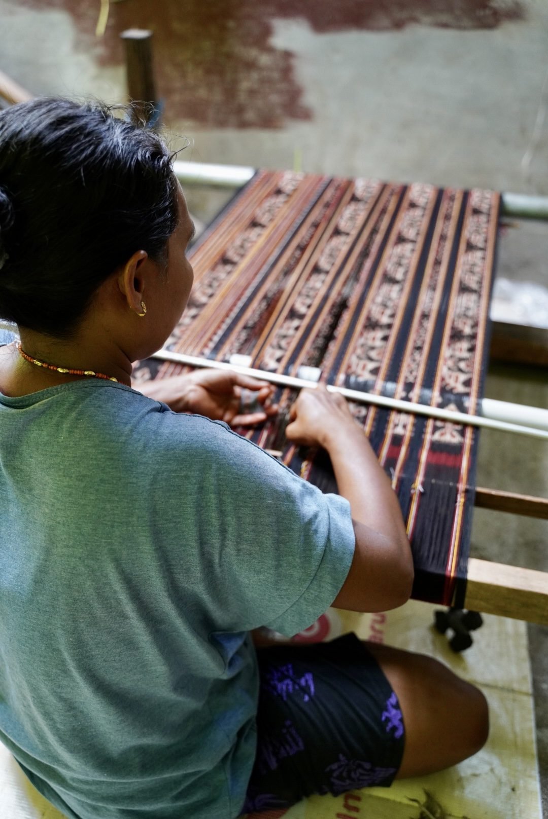 A Mama weaving red ikat on a traditional loom